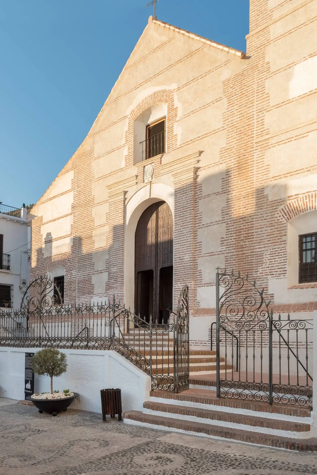 La fachada barroca de pilastras de ladrillo de la Iglesia de San Antonio de Padua en Frigiliana, con el escudo del obispo sobre la portada de arco