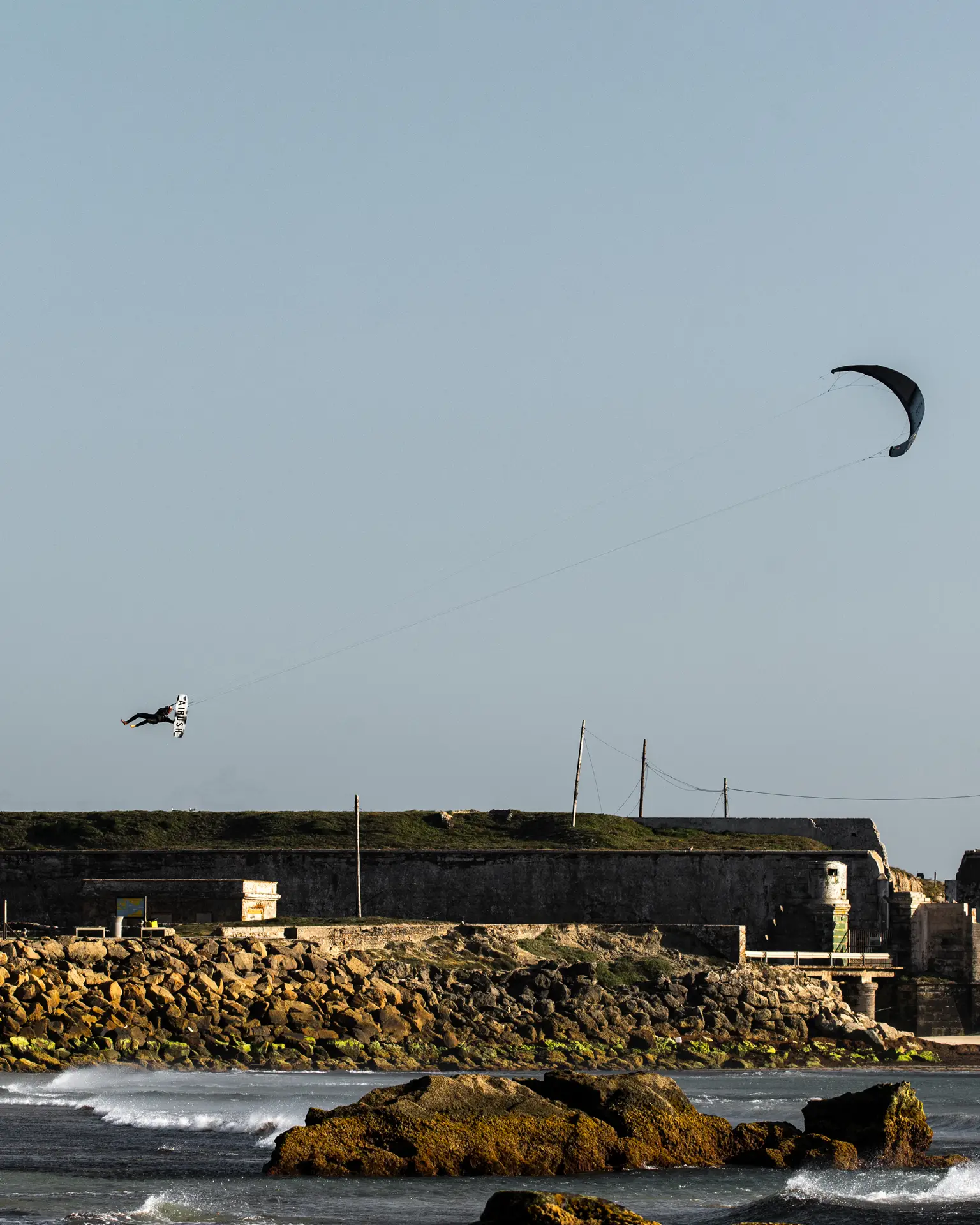 Un kitesurfista saltando alto sobre el agua junto a la fortaleza de la isla de Tarifa
