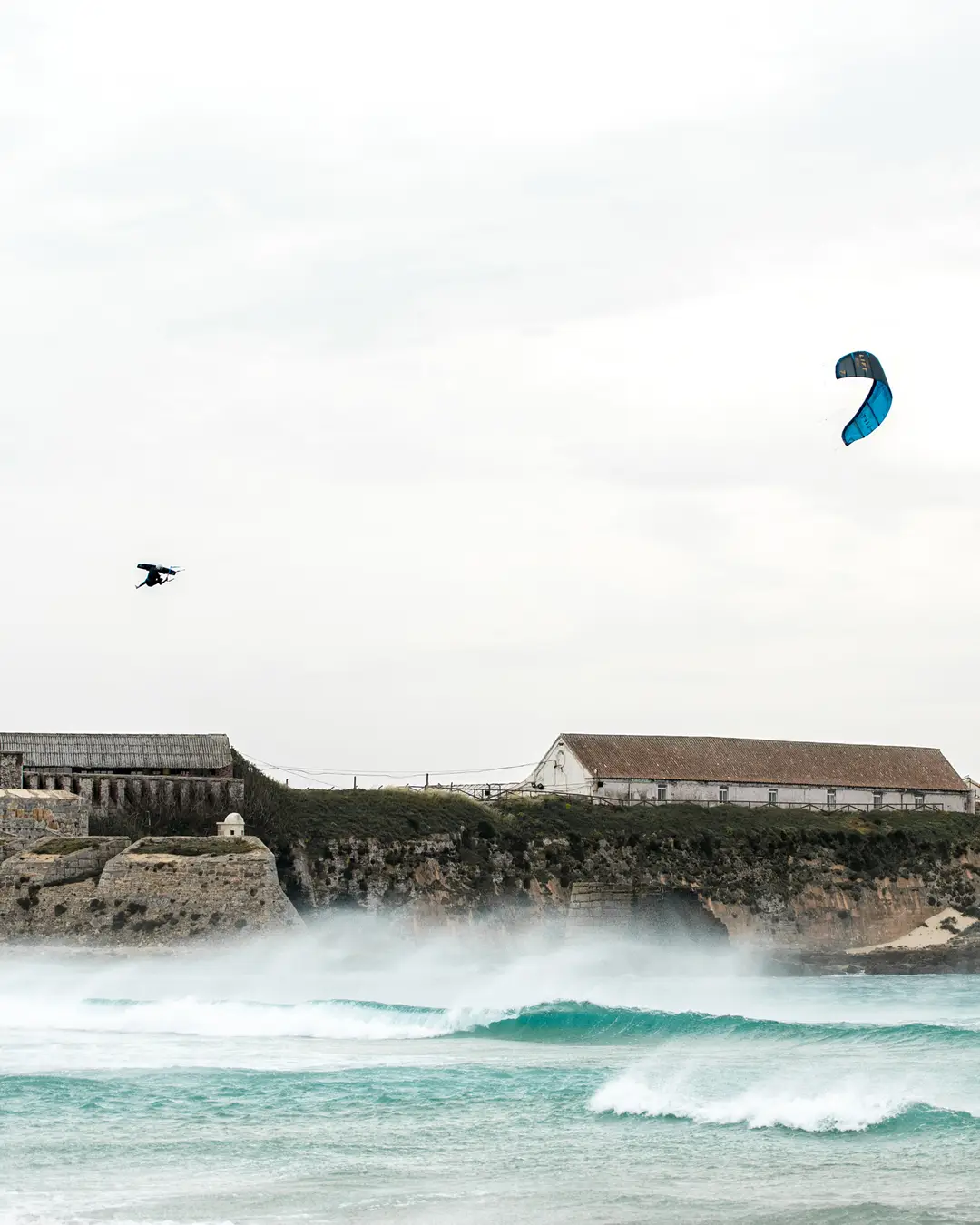 Un kitesurfista muy alto sobre las olas frente a las antiguas naves de la almadraba de Tarifa