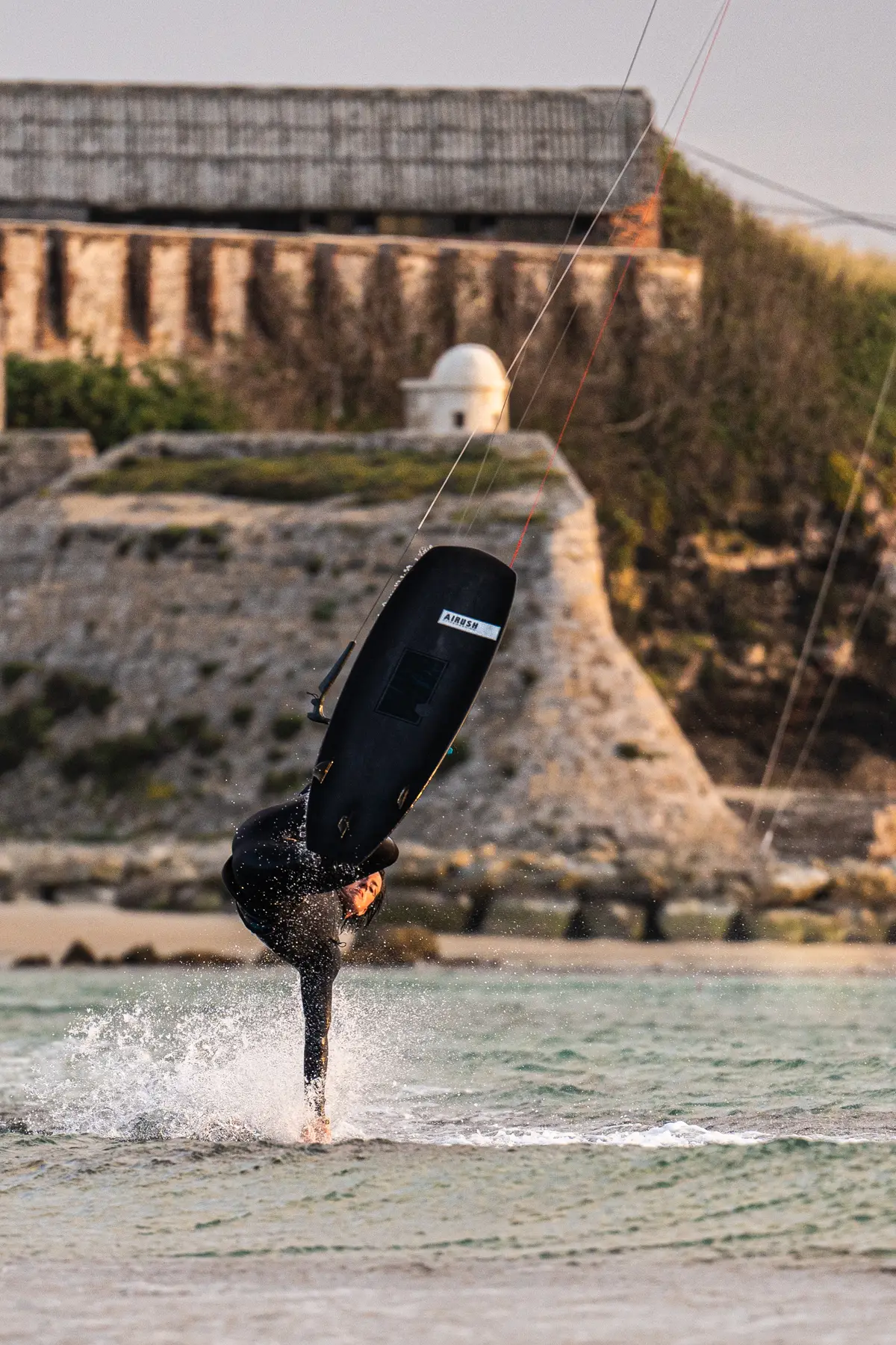 Un kitesurfista con tabla de surf sin straps frente al antiguo fuerte de Tarifa
