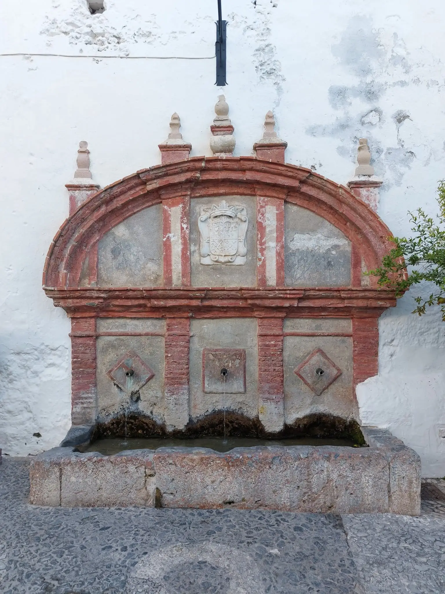 La Fuente Vieja de Frigiliana: un caño de arco de ladrillo con el escudo desgastado de los condes sobre tres surtidores que vierten en un pilón de piedra