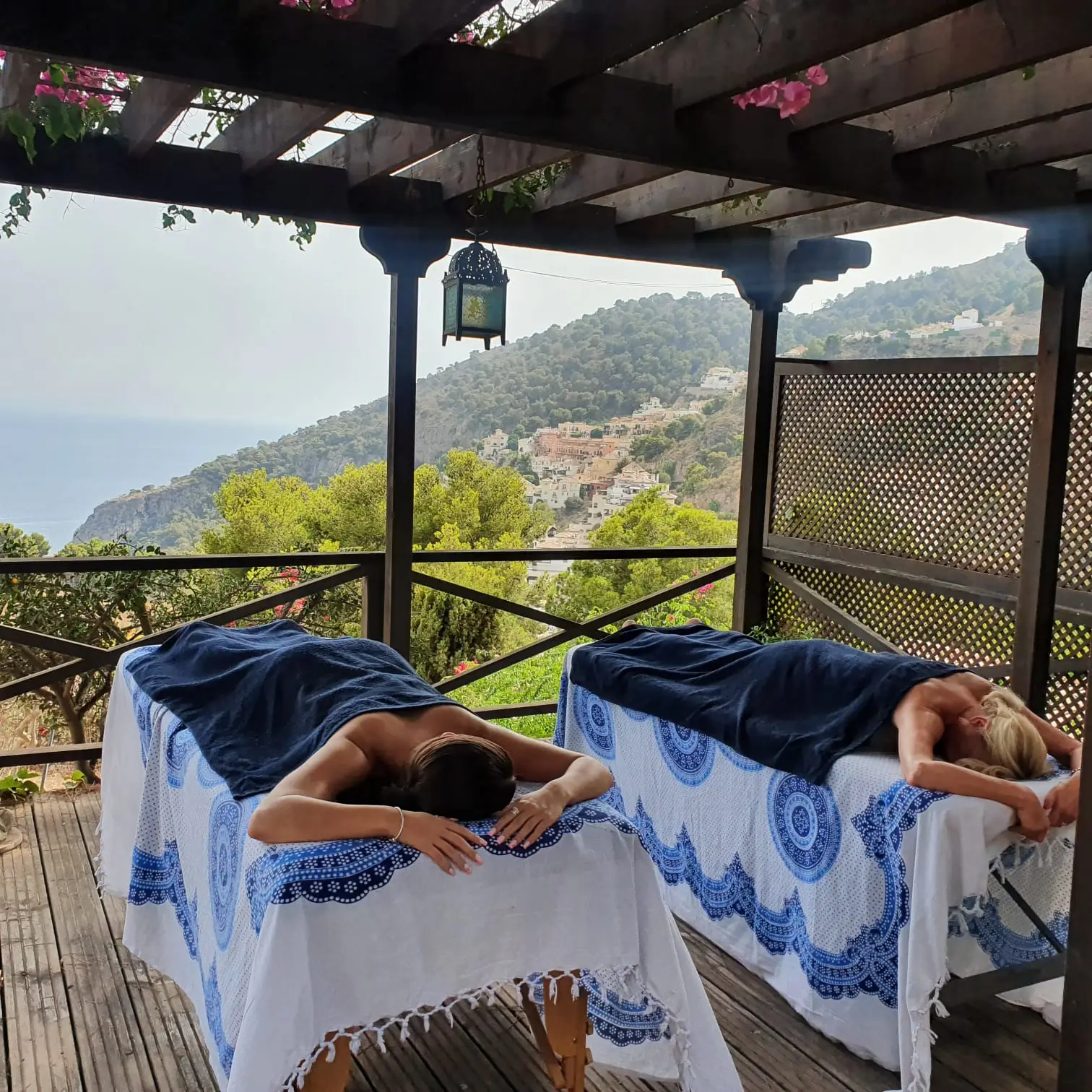 Dos huéspedes en camillas de masaje al aire libre bajo una pérgola con vistas a la montaña cerca de Frigiliana