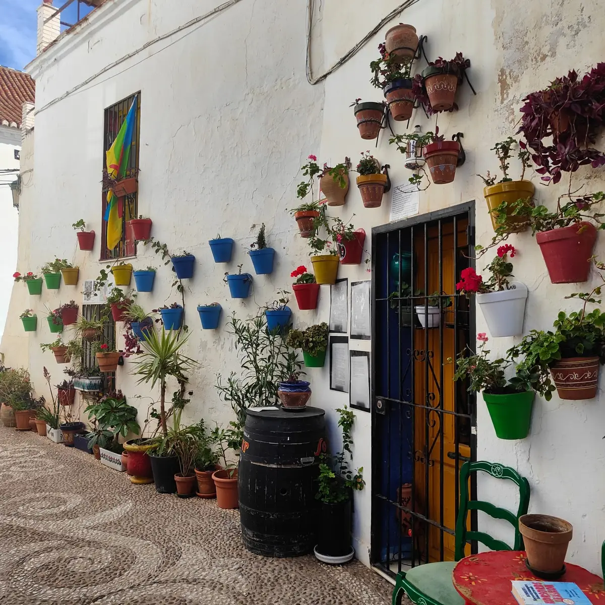 Una callejuela con macetas en una pared blanca y suelo de mosaico de cantos