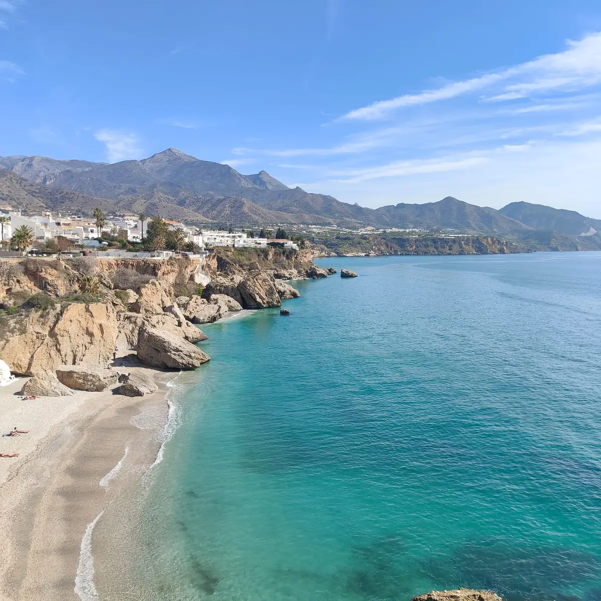 Cala turquesa bajo los acantilados de Nerja vista desde el Balcón de Europa, con la sierra de Almijara al fondo