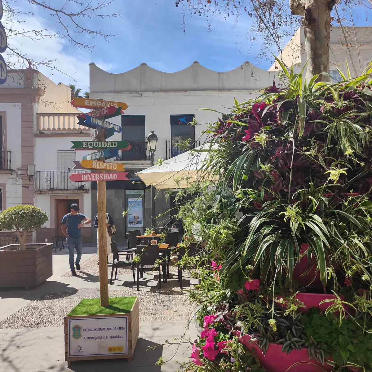 Mesas de café bajo sombrillas en una pequeña plaza de Nerja, con flores en primer plano